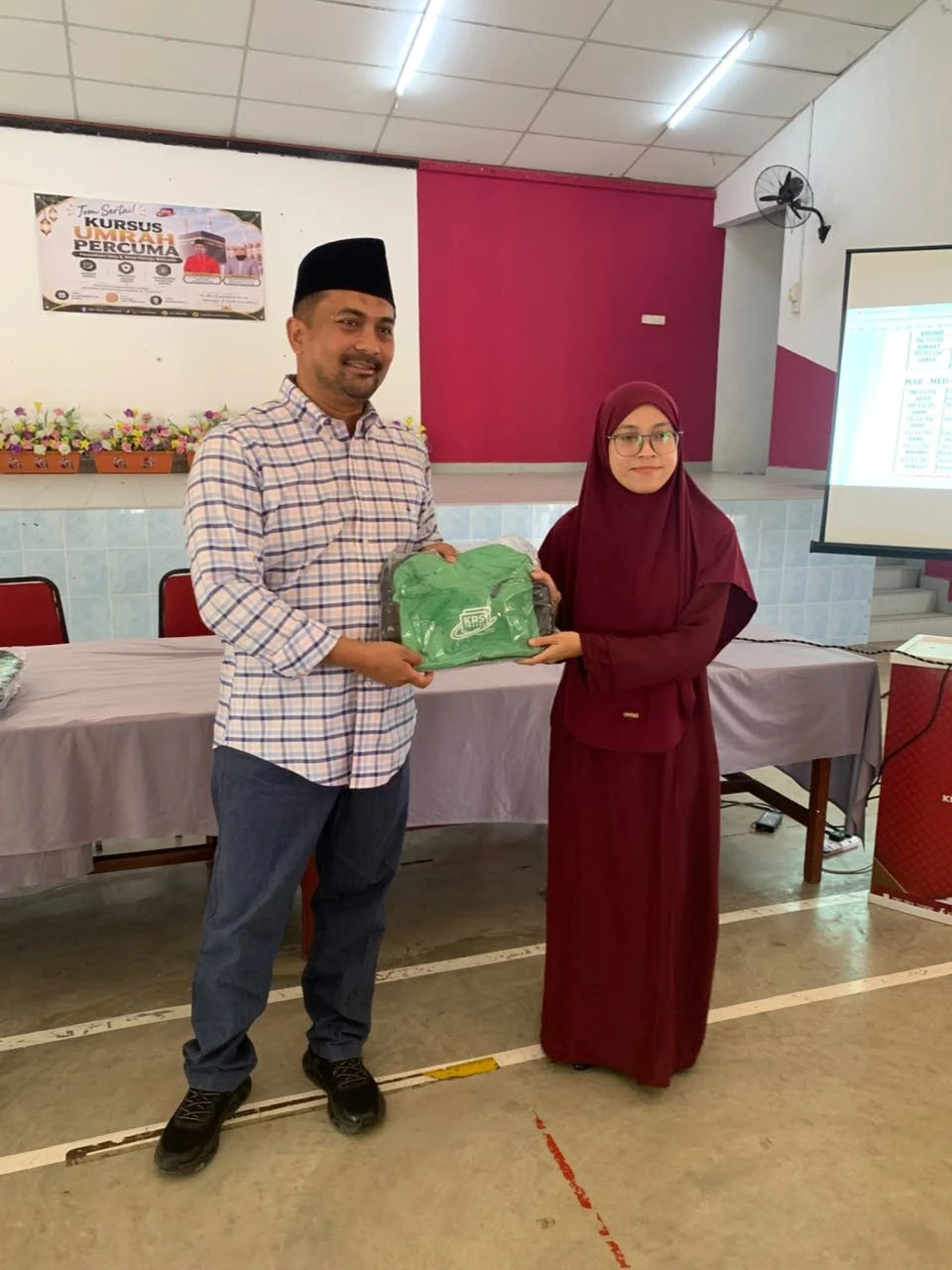 YB Dato’ Mohd Zaidy menyerahkan beg KRS kepada seorang jemaah wanita di hadapan dewan