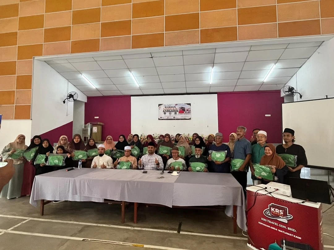 Foto kumpulan peserta kursus umrah mengangkat beg KRS di hadapan banner Kursus Umrah Percuma