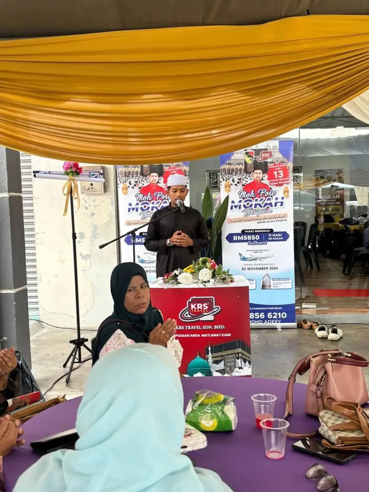 Bacaan doa oleh petugas di podium KRS Travel sementara jemaah menadah tangan di meja jamuan