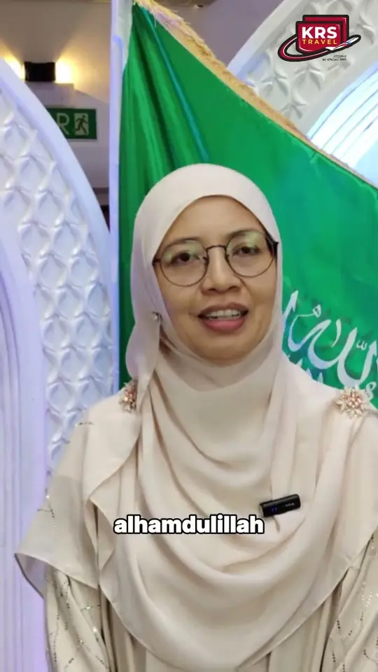 Jemaah haji wanita berbaju kurung krim di hadapan panji hijau majlis haji KRS Travel