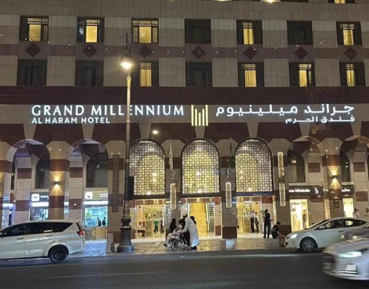 Fasad Grand Millennium Al Haram Hotel di Madinah pada waktu malam, papan tanda hotel bercahaya di atas deretan gerbang pintu masuk