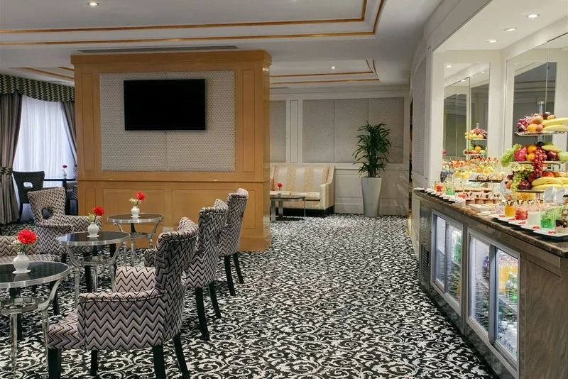 Ruang santai Makkah Hotel dengan kerusi berlapik corak zigzag, meja bulat, paparan buah-buahan dan peti sejuk minuman
