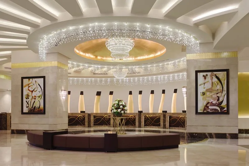 Ruang lobi utama Makkah Hotel dengan candelier kristal besar, kaunter penerimaan tetamu dan kaligrafi berbingkai di dinding